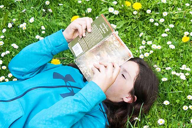 Child laying reading on the grass