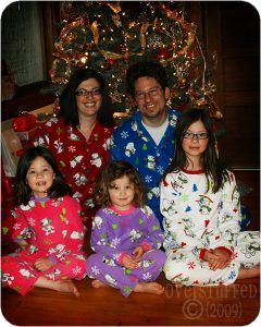 Family wearing matching Christmas pajamas under a Christmas Tree