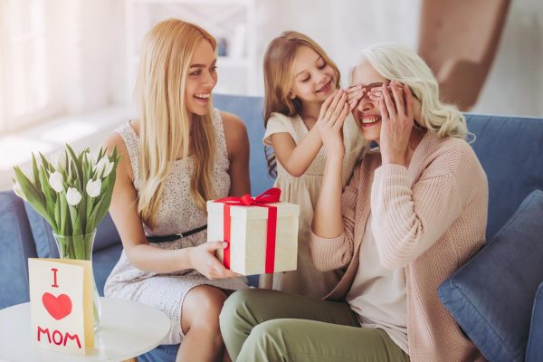 Two daughters surprising their mom with a wrapped gift. I love Mom card in the background.