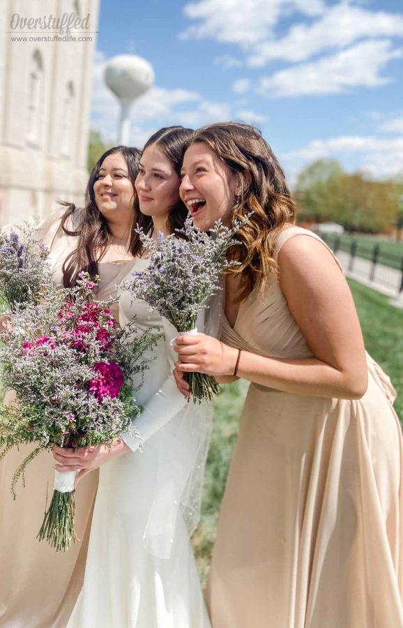 A bride and her two bridesmaids with bouquets, smiling at camera.